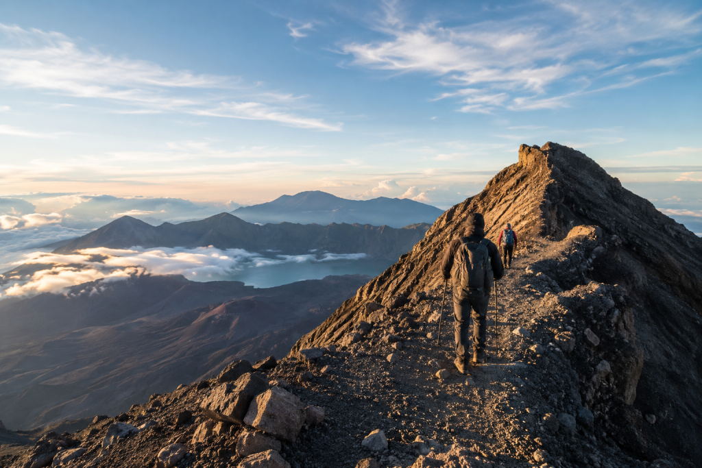 Hikers ascending the final ridge to the Mount Rinjani summit with crater lake and volcanic landscape views in Lombok, Indonesia.