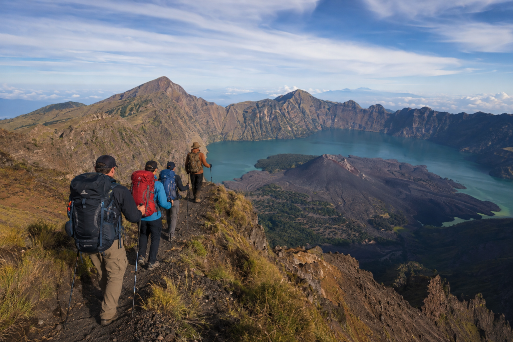 Group of hikers on a Mount Rinjani trekking tour overlooking Segara Anak crater lake and volcanic landscape in Lombok, Indonesia.